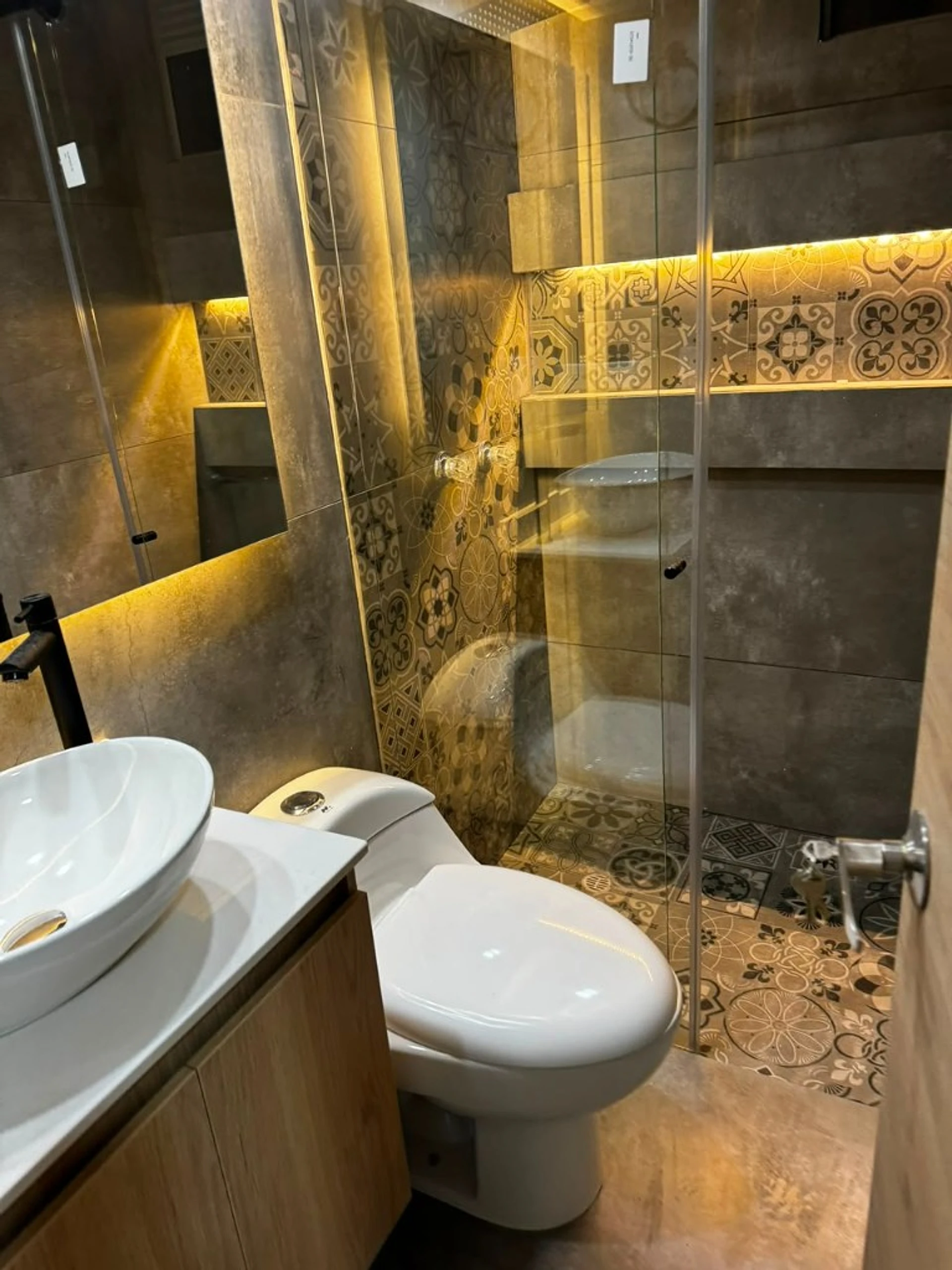 Baño con baldosa en patrón, mampara de vidrio y luz LED