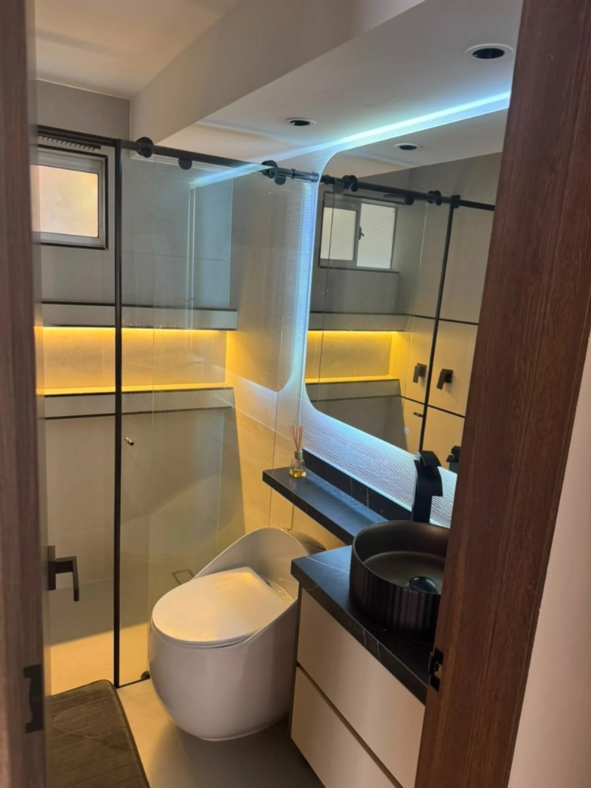 Baño con mampara negra, espejo LED, lavamanos y ducha de vidrio