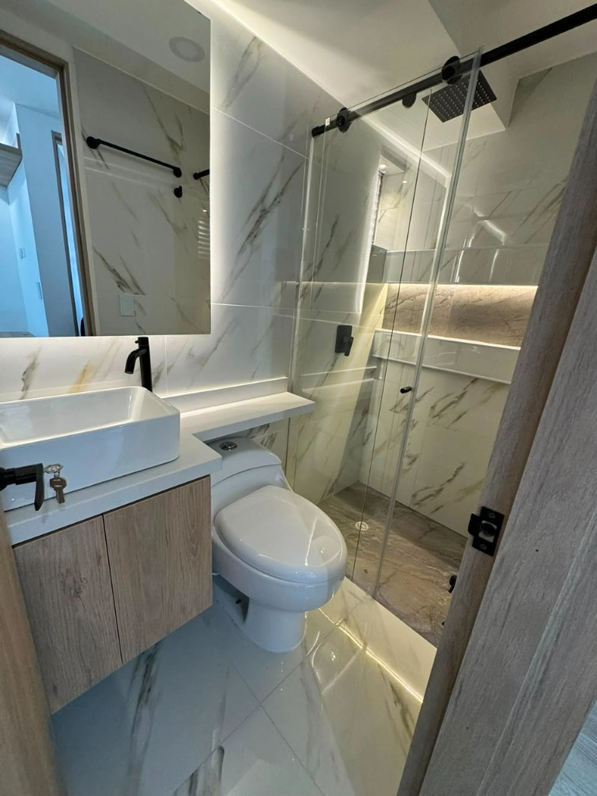 Baño en mármol blanco con grifería negra y ducha corrediza