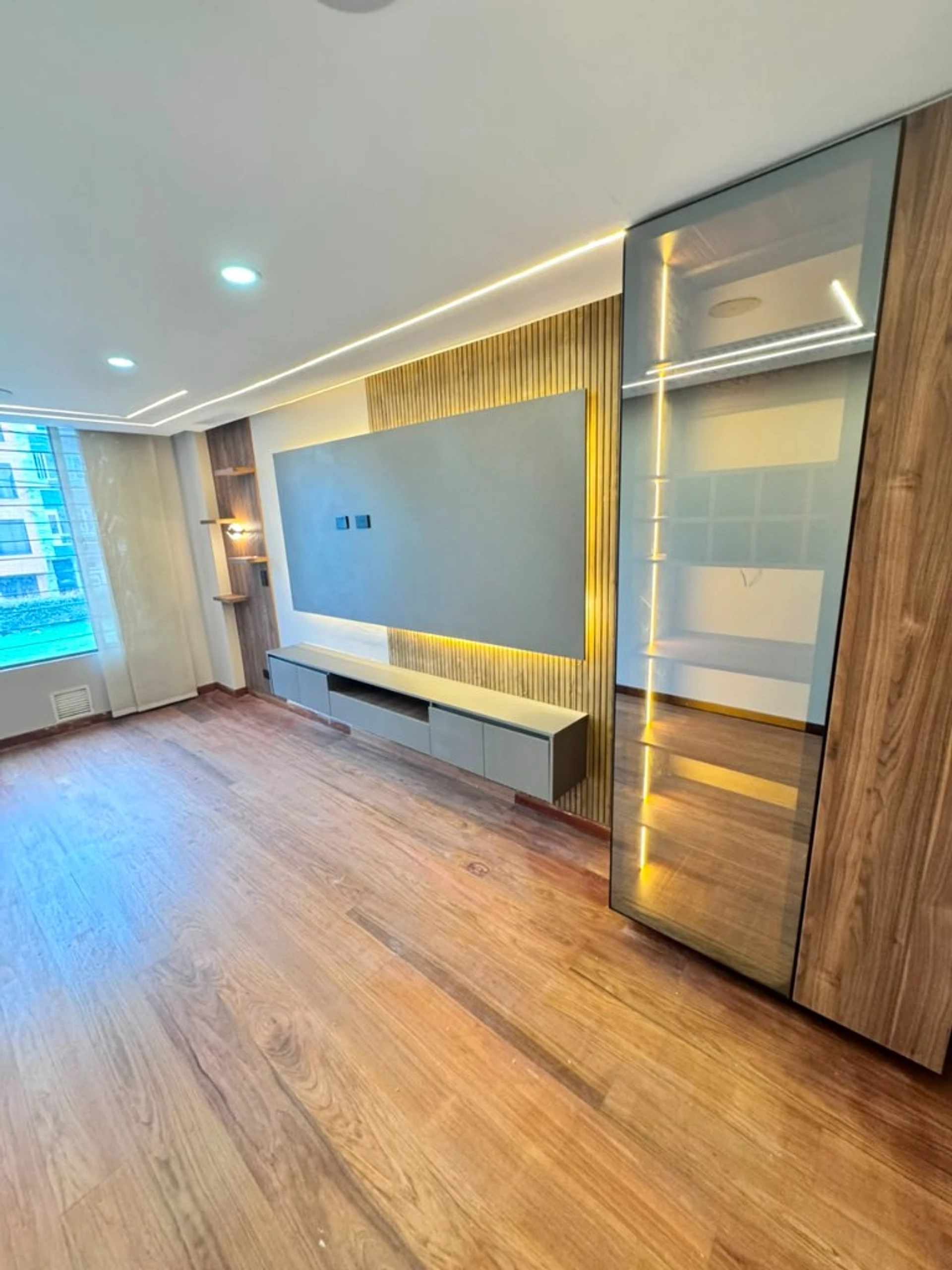 Sala con panel de TV, closet de vidrio iluminado y piso en madera